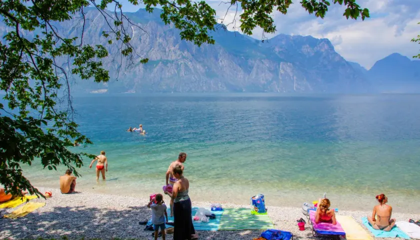 Ludzie odpoczywają na żwirowych plażach nad Jeziorem Garda, podziwiając góry.