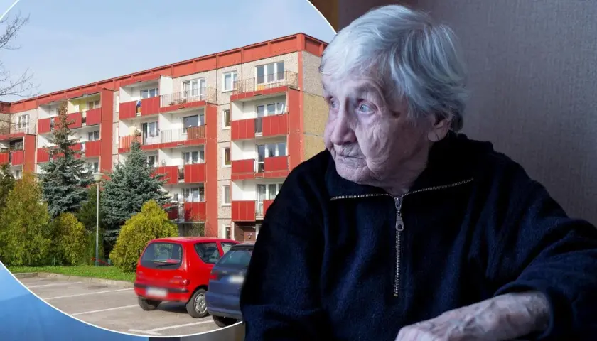 Starsza pani spogląda przez okno na blok mieszkalny, być może zastanawiając się nad swoim dodatkiem mieszkaniowym.