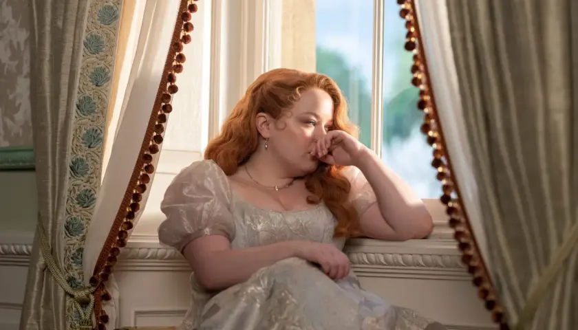 Penelope Bridgerton, la actriz, reflexiona junto a la ventana con un vestido de época.