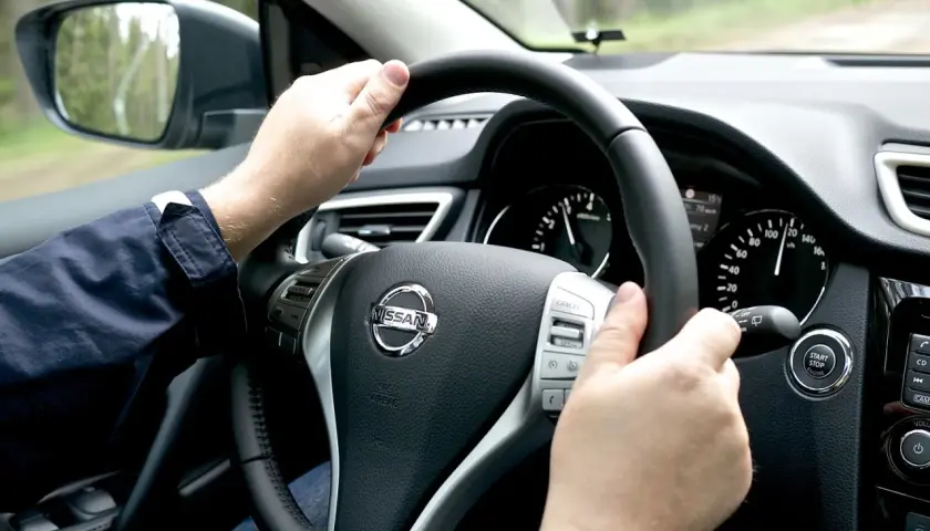 Manos al volante de un Nissan, sintiendo la vibración que indica porque vibra el volante del coche al conducir por un camino rural.