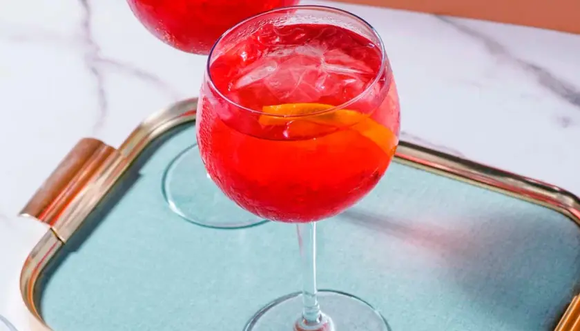 Erfrischender Campari Spritz mit Eis und Orangenscheibe auf einem Tablett.