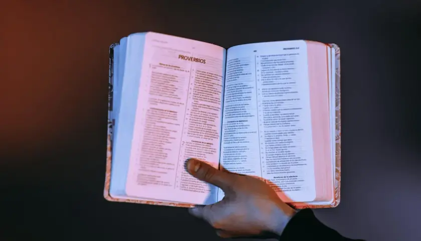 Otwarta księga z tekstem, dłoń przytrzymująca strony. Czy testament bez notariusza jest ważny? Warto szukać odpowiedzi w mądrych księgach.