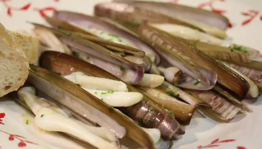 Navajas a la plancha, jugosas y tiernas, servidas con pan y perejil picado. Un manjar marino listo para disfrutar.