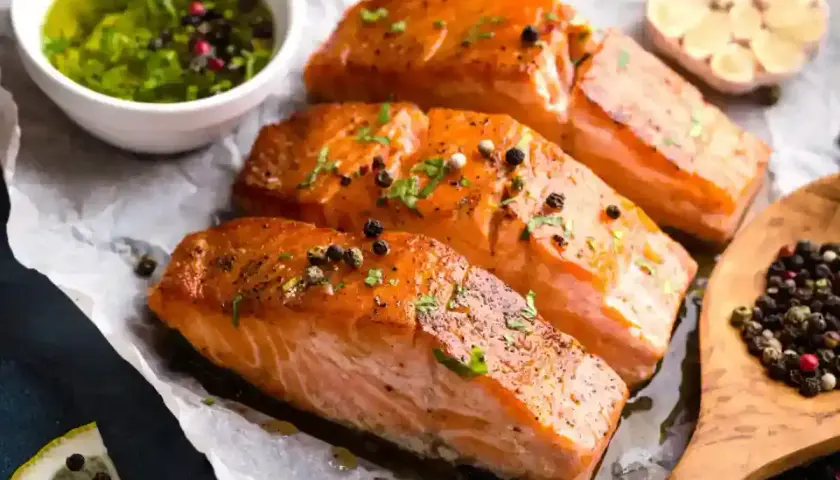 Trois pavés de saumon fumé, parsemés de poivre, accompagnés d'une sauce verte et d'une tête d'ail. Une recette parfaite pour une marinade pour saumon fumé.