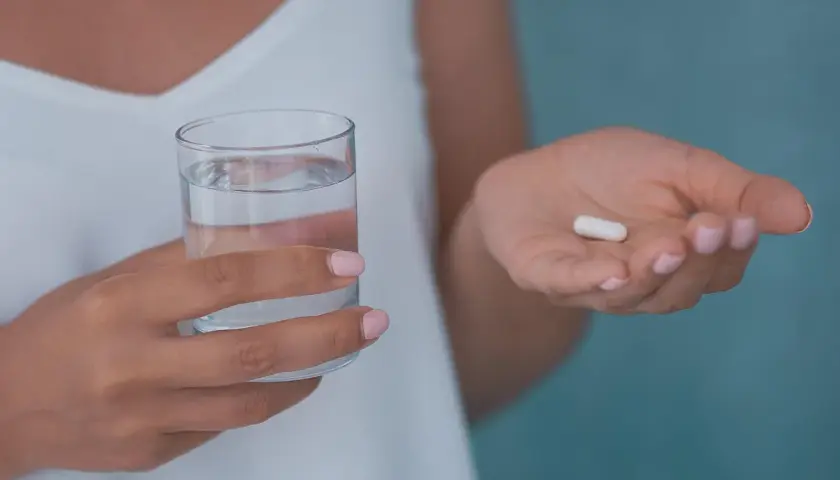 Dłoń trzyma szklankę wody i białą kapsułkę, która może być jednym z neuroleptyków.