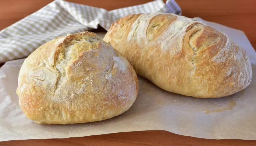 Due pagnotte di pane morbido fatto in casa, dorate e leggermente infarinate, su carta da forno.