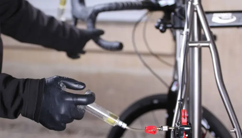 Hands in black gloves perform a bike brake bleed, following the correct brake bleed order to ensure optimal performance.