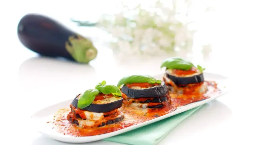 Deliciosas berenjenas a la parmesana, apiladas y cubiertas de salsa de tomate y queso fundido, adornadas con albahaca fresca.