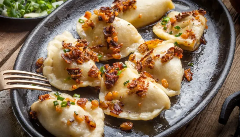 Pyszne pierogi z mięsem, okraszone skwarkami i szczypiorkiem, podane na żeliwnej patelni.
