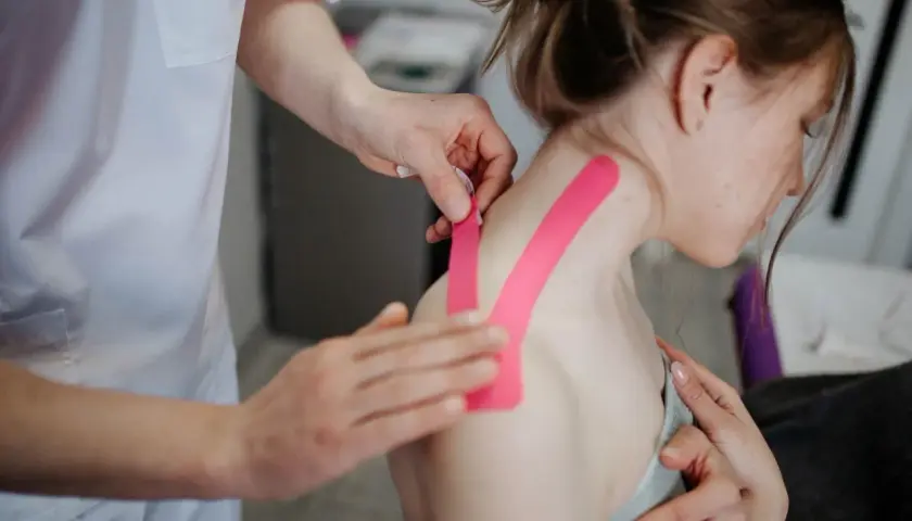 Fisioterapeuta aplica cinta rosa para aliviar dolor de cervicales inflamadas.