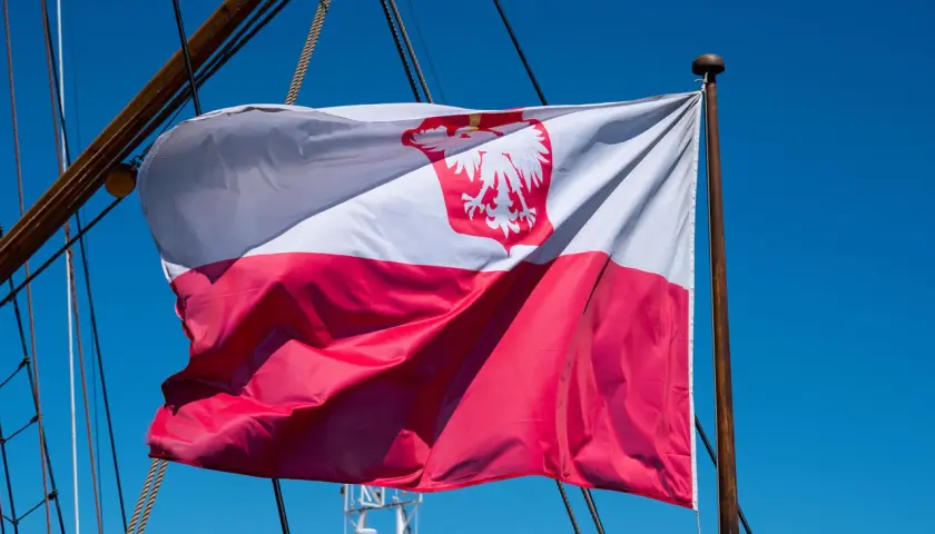 Flaga bandery w Polsce, biało-czerwona z orłem, powiewa na maszcie żaglowca na tle błękitnego nieba.