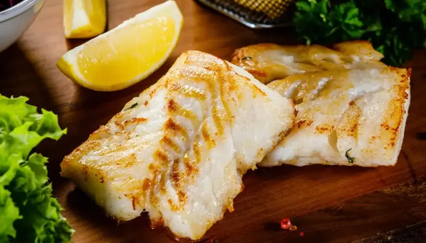 Filetti di branzino in padella in bianco, dorati e succulenti, serviti con spicchi di limone fresco e insalata croccante.