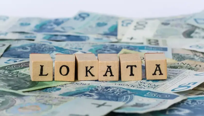 Drewniane klocki z literami "LOKATA" na tle polskich banknotów.