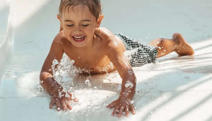 Enfant riant sur un toboggan aquatique, éclaboussures d'eau. Attention aux otites du baigneur symptômes après ces jeux !
