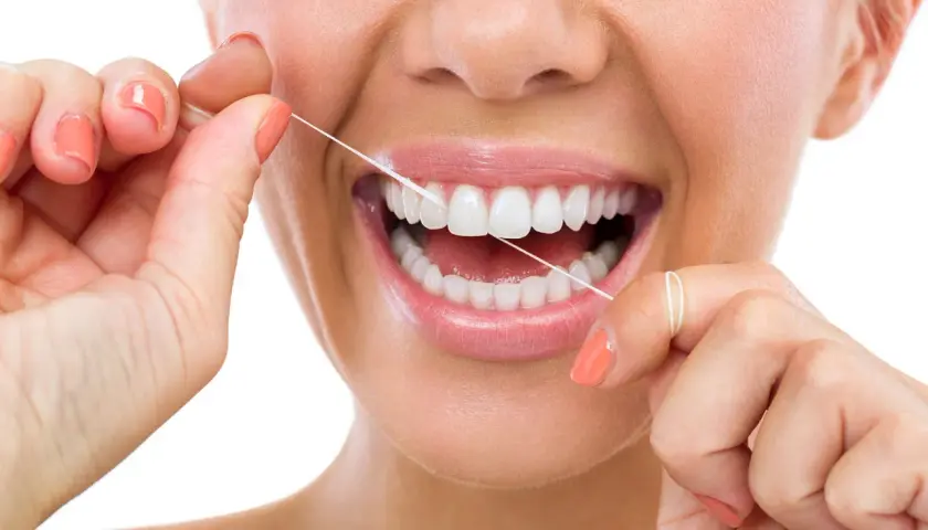 Donna sorride mentre usa il filo interdentale cerato per pulire i suoi denti bianchi e sani.