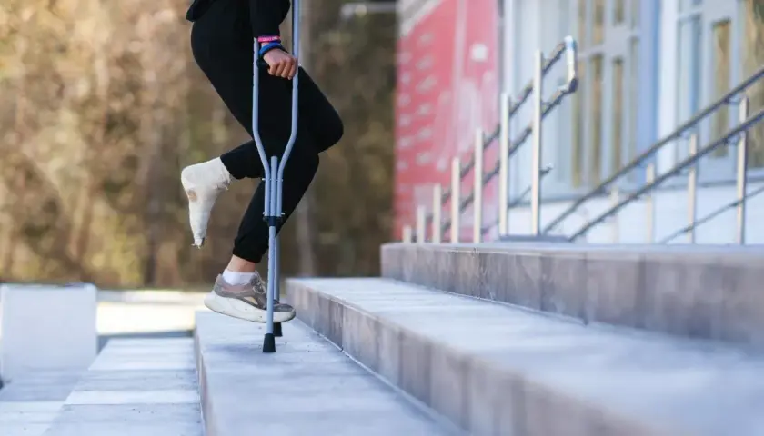 Osoba z zabandażowaną stopą porusza się po schodach, używając kul. W której ręce trzymać kulę, by było najwygodniej?
