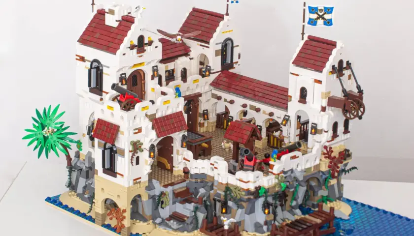 Eine beeindruckende Festung aus moc klemmbausteine, mit Kanonen, Flaggen und einem Steg am blauen Meer.