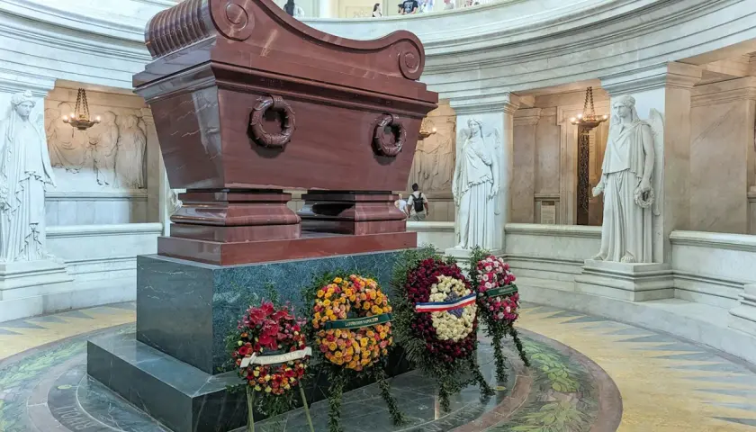 Imponujący sarkofag Napoleona, otoczony rzeźbami i wieńcami, w monumentalnym wnętrzu.