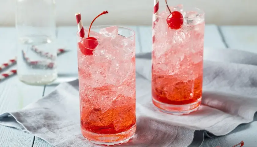 Erfrischende Crodino Rezepte: Zwei Gläser mit Eis, Kirschen und roten Strohhalmen.