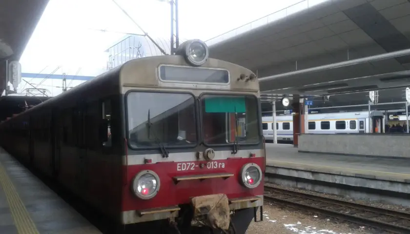 Pociąg ED72-013 ra stoi na peronie. W tle widać nowoczesny budynek dworca i inne pociągi.