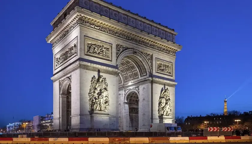 Majestatyczny łuk triumfalny w Paryżu, oświetlony nocą, z wieżą Eiffla w oddali.