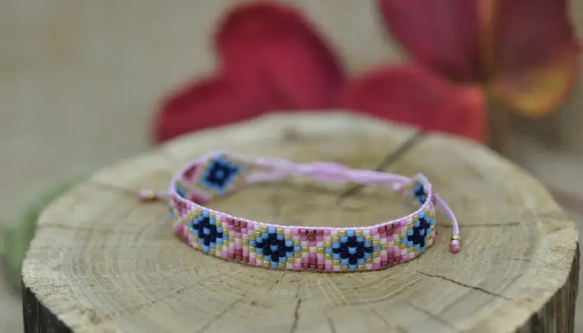 Kolorowa bransoletka z koralików diy, ozdobiona geometrycznym wzorem, spoczywa na drewnianym plastrze.