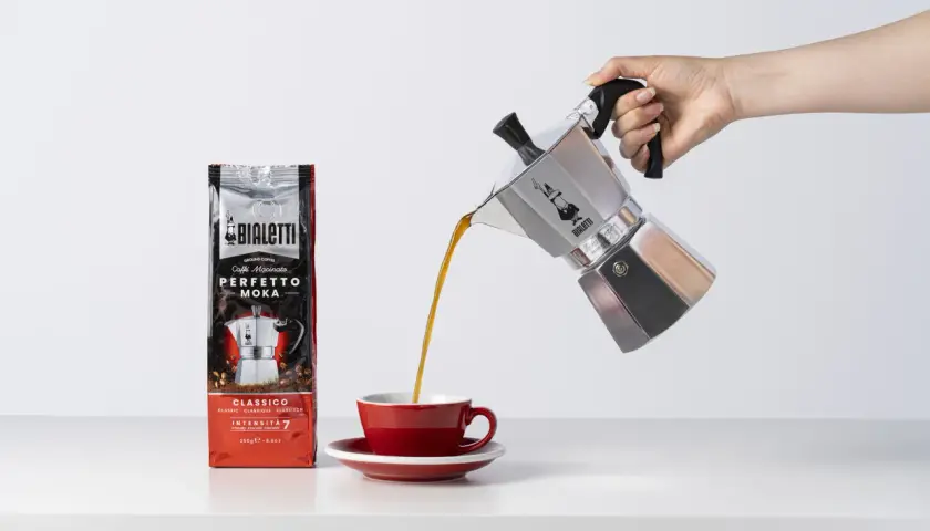 Aromatyczne espresso z kawiarki Bialetti trafia do czerwonej filiżanki. Obok stoi paczka kawy Perfetto Moka.