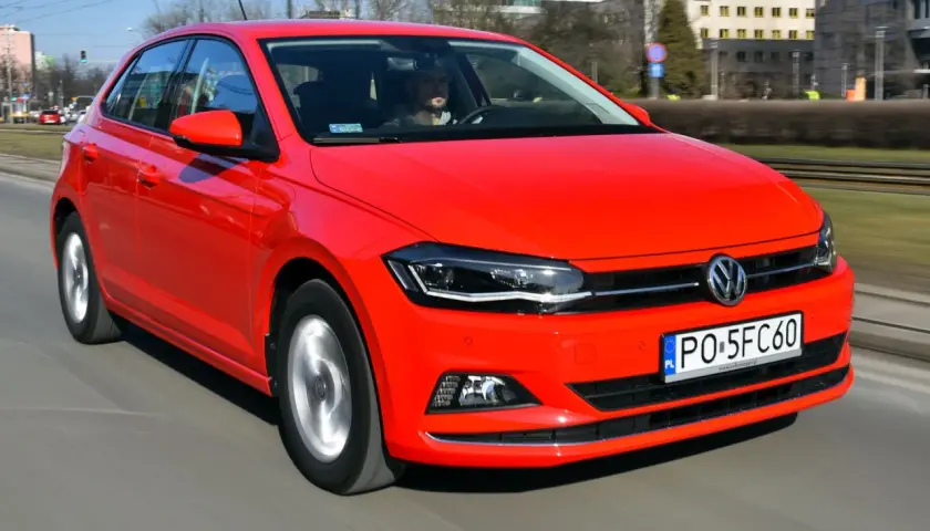 Czerwony Volkswagen Polo 6 w ruchu miejskim. Kierowca w okularach przeciwsłonecznych prowadzi auto po ulicy.