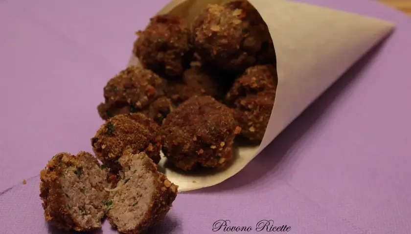 Un cono di carta pieno di polpette fritte dorate, una tagliata a metà rivela un interno succoso.