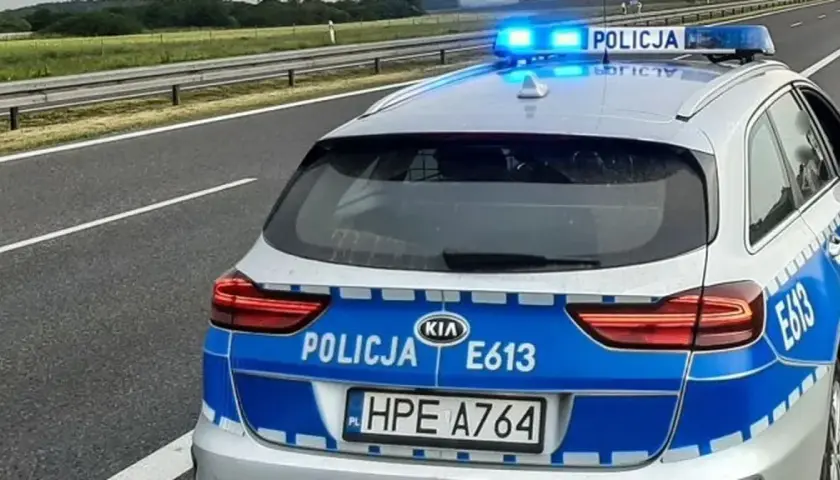 Policyjny pojazd uprzywilejowany z włączonymi niebieskimi światłami stoi na poboczu autostrady.
