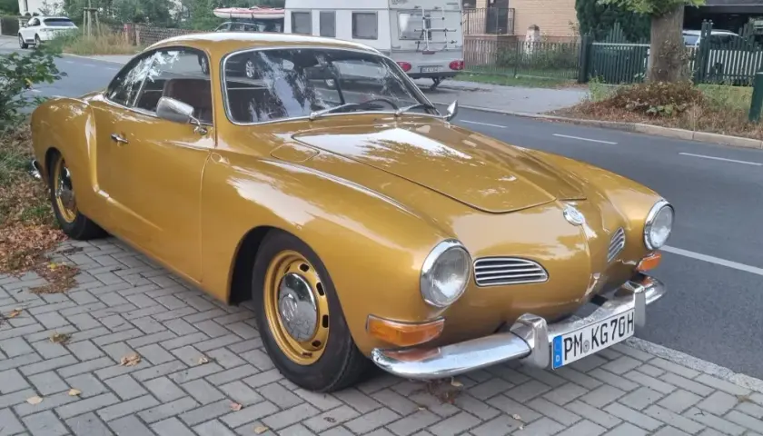 Złoty Karmann Ghia, klasyk z lat 60., lśni na tle ulicy.