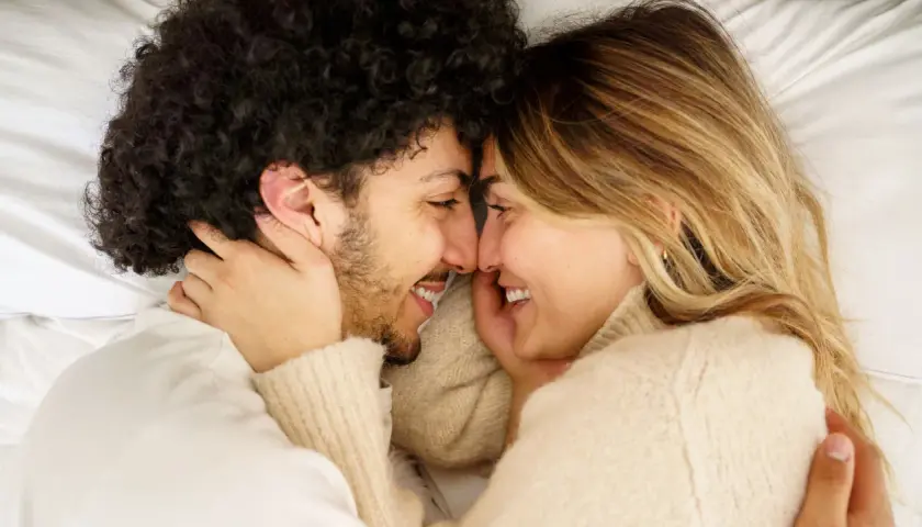 Coppia in un abbraccio intimo, sorrisi e sguardi complici. Un momento di tenerezza e sesso a coppia che celebra l'amore.