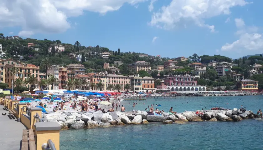 Plage animée à Santa Margherita Ligure, Italie, avec des parasols colorés, des baigneurs sur les rochers et des bâtiments pittoresques à flanc de colline.