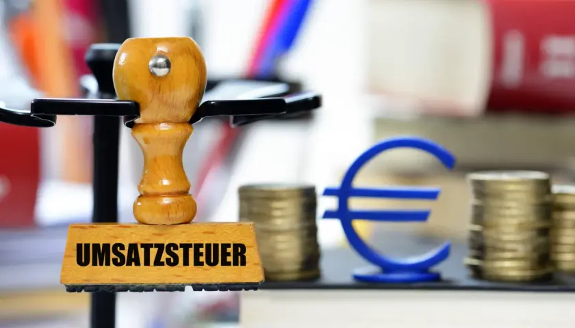 Stempel mit "Umsatzsteuer" und Euro-Symbol, Münzstapel und Bücher. Symbolisiert die regelbesteuerung landwirtschaft.