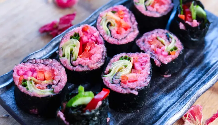 Sushi rolls with vibrant pink rice, filled with fresh vegetables like cucumber and red pepper. A delightful pink rice recipe for a colorful meal.