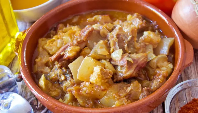 Guiso de cap i pota en cazuela de barro, con patatas y trozos de carne, acompañado de ingredientes frescos.