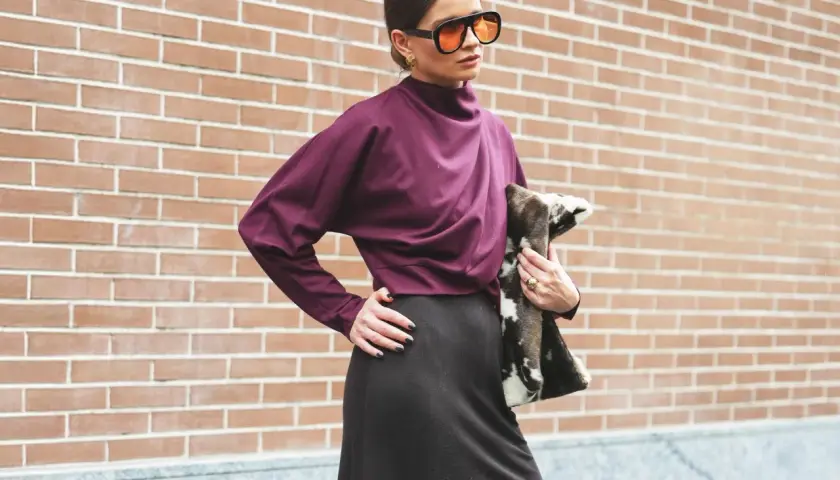Mujer con gafas naranjas y blusa color burdeos, posando con un bolso de pelo.