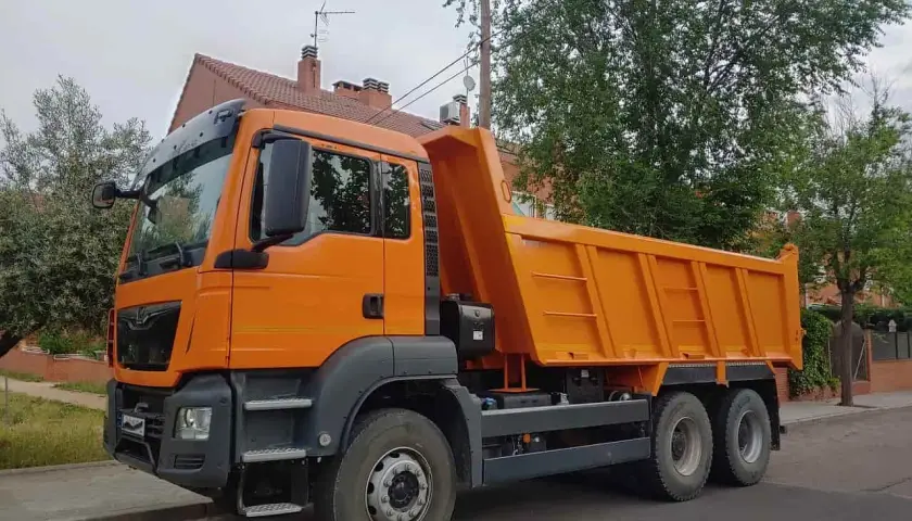 Pomarańczowa wywrotka, idealna do transportu materiałów budowlanych. Z kategorią C można ciągnąć taką przyczepę.