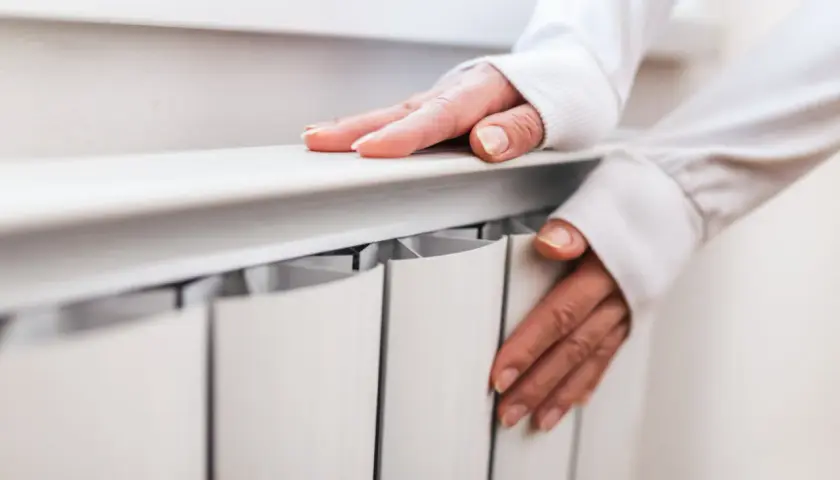 Dłonie na grzejniku, sprawdzające temperaturę. Czas pomyśleć, kiedy wyłączyć ogrzewanie podłogowe.