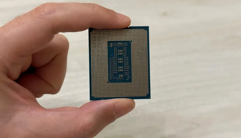 Un dedo sostiene un microprocesador, mostrando su intrincado diseño de pines dorados y el chip central.