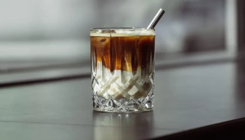 Eiskaffee selber machen ohne Vanilleeis: Ein Glas mit geschichtetem Kaffee und Milch, garniert mit einem Metallstrohhalm.