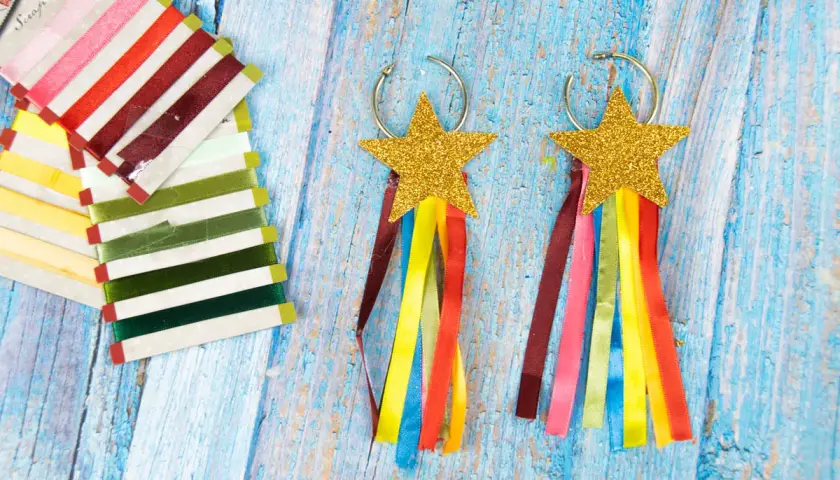 Aretes de carnaval manualidades con estrellas doradas y cintas de colores. Un conjunto de cintas de raso de varios tonos a la izquierda.