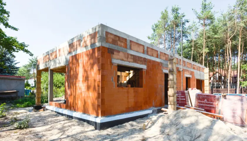 Budowa domu z pustaków ceramicznych. Widać fundamenty, ściany z otworami okiennymi i drzwiowymi. To początek realizacji projektów domów bez pozwolenia.