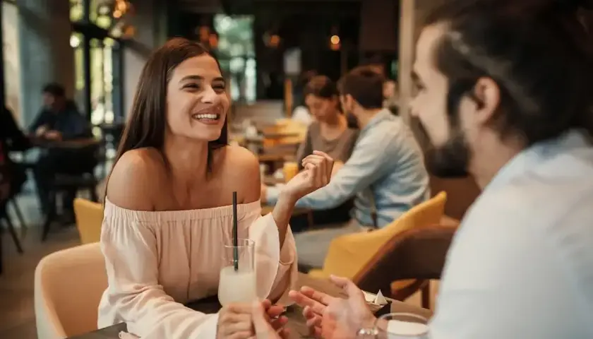 Uśmiechnięta para rozmawia w kawiarni. On zastanawia się, jak zaprosić dziewczynę na wesele.