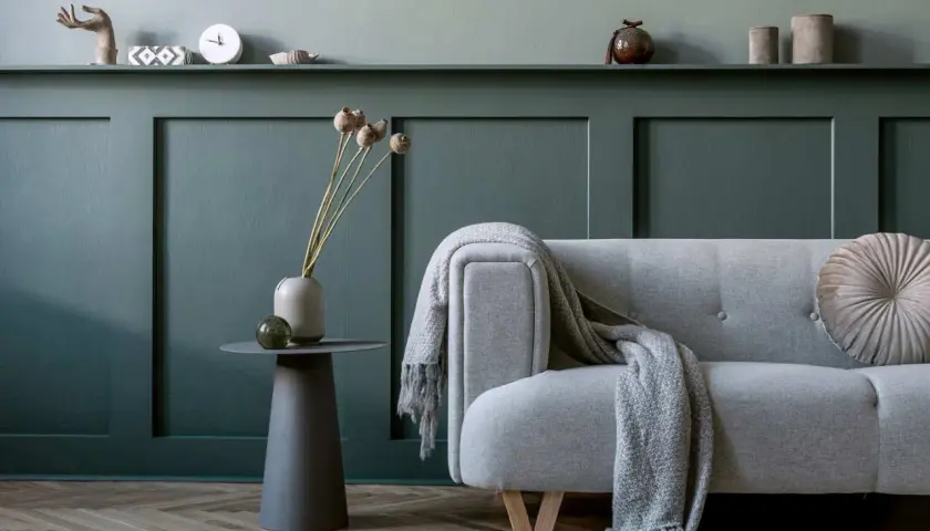Divano grigio con coperta, vaso con fiori secchi e tavolino su parete con boiserie fai da te.