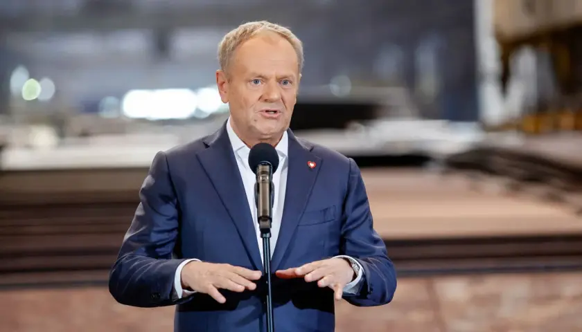 Donald Tusk w garniturze przemawia przy mikrofonie.