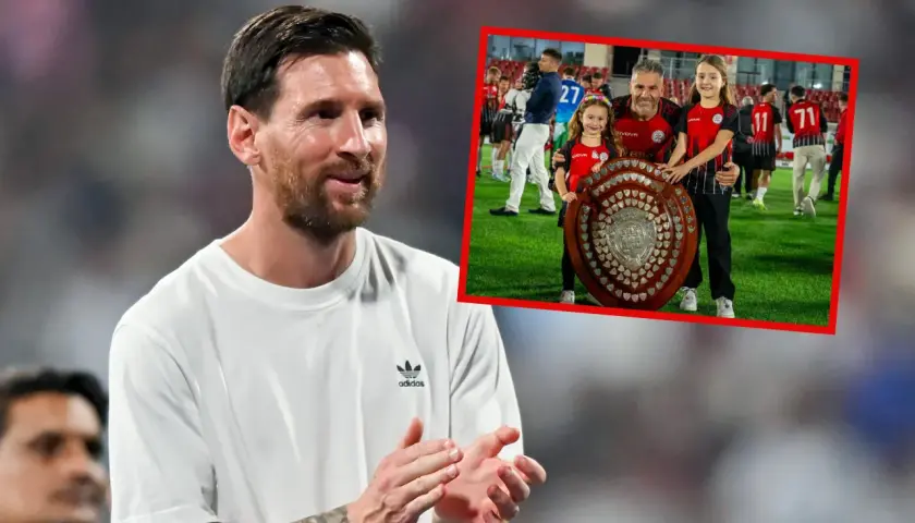 Lionel Messi, najbardziej utytułowany piłkarz w historii, uśmiecha się, podczas gdy w tle widać jego drużynę świętującą z pucharem.