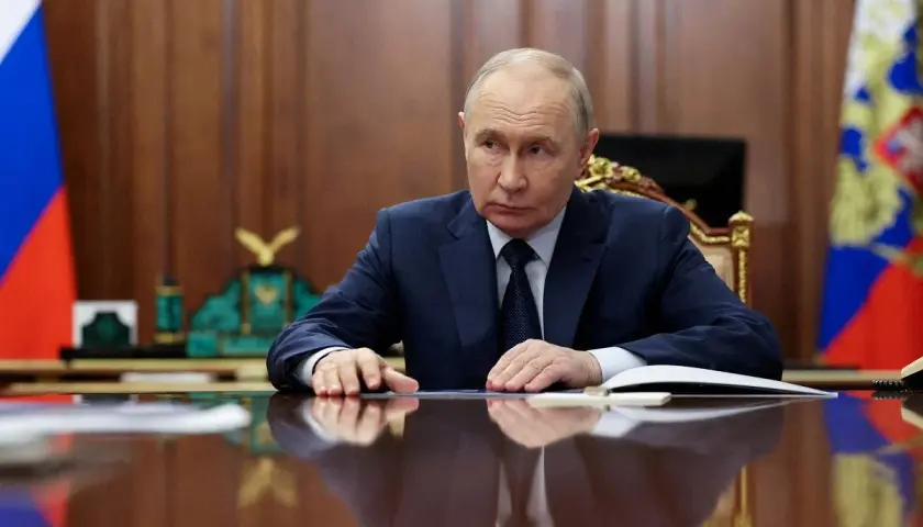 Władimir Putin siedzi przy biurku, zamyślony. Za nim rosyjskie flagi. Czeka na nas świat.