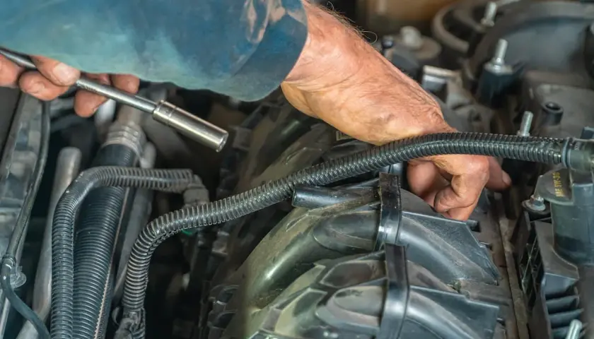 Mechanik z kluczem nasadowym pracuje przy silniku samochodu, demontując elementy układu paliwowego.