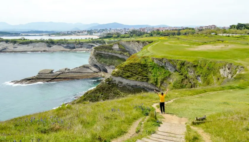 Persona con los brazos en alto en un acantilado verde, contemplando el mar y la costa. ¡Ideas para que ver en Cantabria en 4 días!